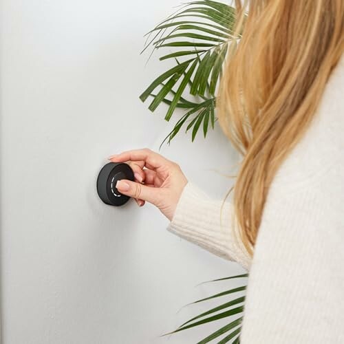Person adjusting a smart thermostat on a wall.